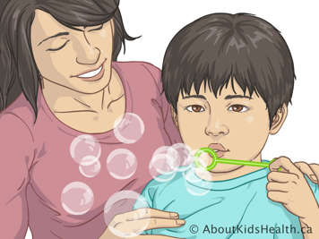 Niño pequeño soplando burbujas mientras su madre lo mira sonriente con las manos apoyadas sobre los hombros del niño