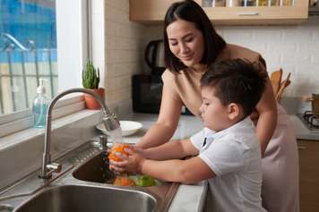 Woman and school-age boy washing oranges and apples at a kitchen sink