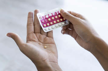 Hand holding pack of birth control pills and tablets