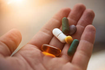 Hand holding various vitamin pills and tablets