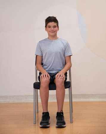 boy sitting in chair with back straight and hands on knees