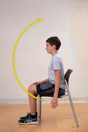 Side view of boy sitting upright in chair with arm by his side